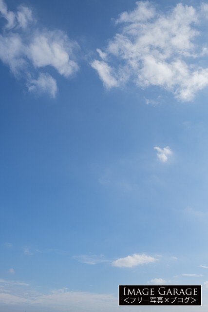 下に小さめ上に大きめの雲がある青空（縦）のフリー写真素材（無料）