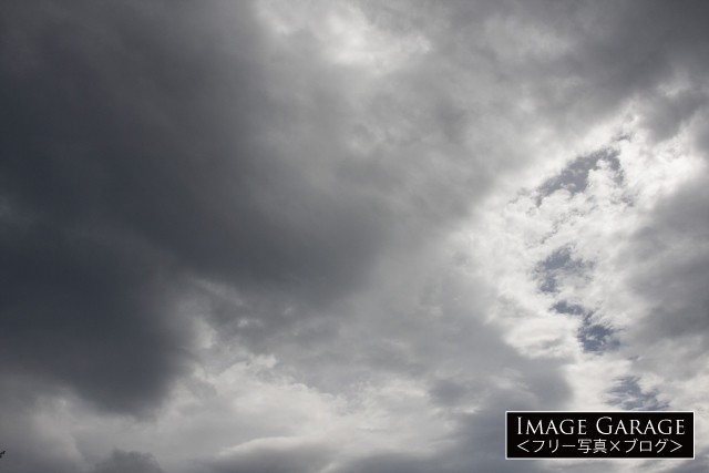 黒い雲が覆いながら光が差し込む曇り空のフリー画像
