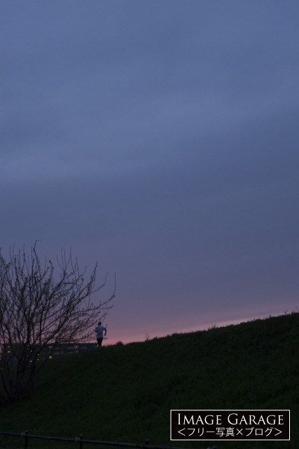 夕暮れ時の鶴見川の土手とランナーのフリー写真素材（無料画像）