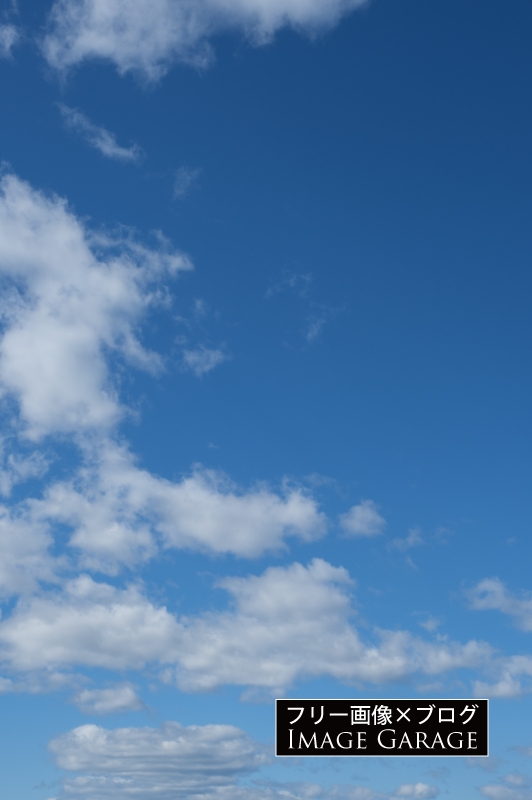 左下のに綿のような雲がある青空（縦）のフリー写真素材（無料画像）