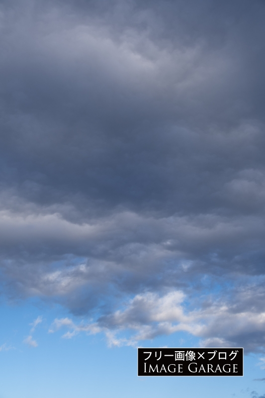 暗めの厚い雲あある青空（縦）のフリー写真素材（無料画像）