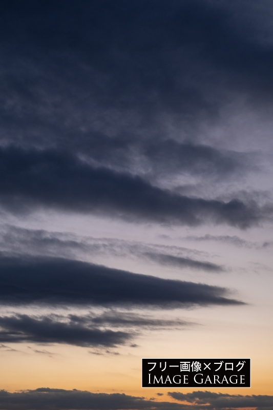 夕焼け空と流れるような黒い雲（縦）のフリー写真素材（無料画像）